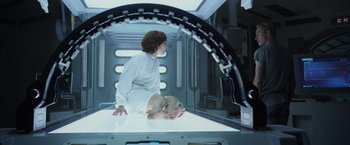 Movie still from “Prometheus” (2012), directed by Ridley Scott – A woman sitting on top of a table in a room; Wide shot, Low angle