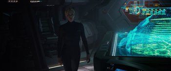 Movie still from “Prometheus” (2012), directed by Ridley Scott – A woman standing in a dark room next to a table; Medium shot, Over the shoulder angle