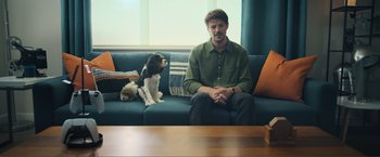 Movie still from “Puppy Love” (2023), directed by Richard Alan Reid – A man sitting on top of a couch next to a dog; Wide shot, Over the shoulder angle