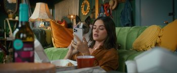 Movie still from “Puppy Love” (2023), directed by Richard Alan Reid – A woman sitting on a couch looking at a phone; Medium shot, High angle