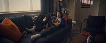 Movie still from “Puppy Love” (2023), directed by Richard Alan Reid – A man sitting on top of a couch next to a dog; Wide shot, High angle