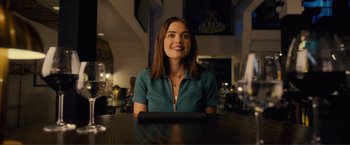 Movie still from “Puppy Love” (2023), directed by Richard Alan Reid – A woman sitting at a table in front of a laptop computer; Medium shot, Over the shoulder angle