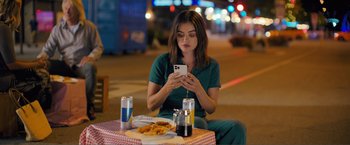 Movie still from “Puppy Love” (2023), directed by Richard Alan Reid – A woman sitting at a table with a plate of food and a cell phone; Medium shot, High angle