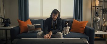 Movie still from “Puppy Love” (2023), directed by Richard Alan Reid – A man sitting on top of a couch next to a dog; Wide shot, Low angle