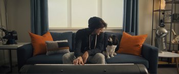 Movie still from “Puppy Love” (2023), directed by Richard Alan Reid – A man sitting on a couch next to a dog; Medium shot, Low angle