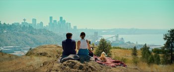 Movie still from “Puppy Love” (2023), directed by Richard Alan Reid – Two people and a dog sitting on top of a hill overlooking a city; Extreme Wide shot, High angle