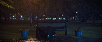 Movie still from “Puppy Love” (2023), directed by Richard Alan Reid – A person sitting under an umbrella on top of a park bench; Extreme Wide shot, Low angle