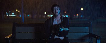 Movie still from “Puppy Love” (2023), directed by Richard Alan Reid – A man sitting on top of a wooden bench holding a dog; Medium shot, High angle