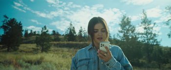Movie still from “Puppy Love” (2023), directed by Richard Alan Reid – A woman holding a cell phone while standing in a field; Close Up shot, High angle