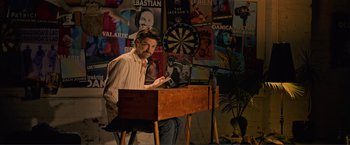 Movie still from “Puppy Love” (2023), directed by Richard Alan Reid – A man sitting in front of a wooden desk; Medium shot, Low angle