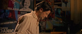 Movie still from “Puppy Love” (2023), directed by Richard Alan Reid – A man in a striped shirt is speaking into a microphone; Medium shot, Low angle