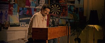 Movie still from “Puppy Love” (2023), directed by Richard Alan Reid – A man standing at a podium in front of a microphone; Medium shot, Over the shoulder angle