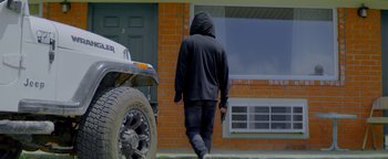 Movie still from “Pursuit” (2022), directed by Brian Skiba – A man in a black hoodie walking in front of a brick building; Wide shot, Low angle