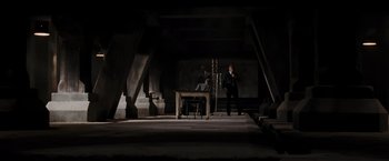 Movie still from “Quantum of Solace” (2008), directed by Marc Forster – Two men sitting at a table in a dark room; Extreme Wide shot, Low angle