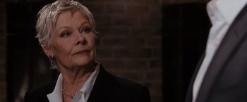 Movie still from “Quantum of Solace” (2008), directed by Marc Forster – An older woman wearing a suit and a necklace; Close Up shot, Low angle