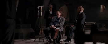 Movie still from “Quantum of Solace” (2008), directed by Marc Forster – A man sitting on a chair in front of two other men; Wide shot, High angle