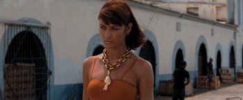Movie still from “Quantum of Solace” (2008), directed by Marc Forster – A woman wearing a gold necklace and a brown dress; Close Up shot, Low angle