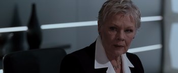 Movie still from “Quantum of Solace” (2008), directed by Marc Forster – An older woman in a black suit and white shirt; Close Up shot, Over the shoulder angle