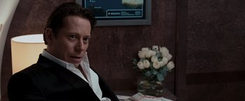 Movie still from “Quantum of Solace” (2008), directed by Marc Forster – A man sitting in front of a tv and a bunch of flowers; Close Up shot, Over the shoulder angle