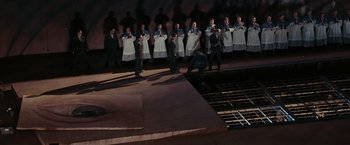 Movie still from “Quantum of Solace” (2008), directed by Marc Forster – A group of men standing next to each other on a stage; Extreme Wide shot, High angle