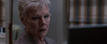 Movie still from “Quantum of Solace” (2008), directed by Marc Forster – An older woman with short white hair looking at the camera; Close Up shot, Over the shoulder angle