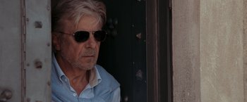 Movie still from “Quantum of Solace” (2008), directed by Marc Forster – An older man wearing sunglasses and a blue shirt; Close Up shot, Over the shoulder angle