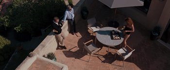 Movie still from “Quantum of Solace” (2008), directed by Marc Forster – Two men standing in an outdoor area with an umbrella; Wide shot, High angle