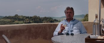 Movie still from “Quantum of Solace” (2008), directed by Marc Forster – An older man sitting at a table eating a sandwich; Medium shot, Low angle