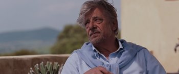 Movie still from “Quantum of Solace” (2008), directed by Marc Forster – An older man with grey hair and a blue shirt is sitting outside; Close Up shot, Over the shoulder angle