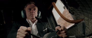 Movie still from “Quantum of Solace” (2008), directed by Marc Forster – A man wearing a suit and tie while holding a steering wheel; Close Up shot, Low angle