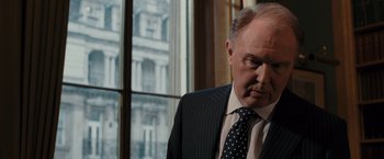 Movie still from “Quantum of Solace” (2008), directed by Marc Forster – An older man in a suit and tie looking out of a window; Close Up shot, Over the shoulder angle