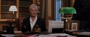 Movie still from “Quantum of Solace” (2008), directed by Marc Forster – An older woman sitting in front of a laptop computer; Medium shot, Low angle