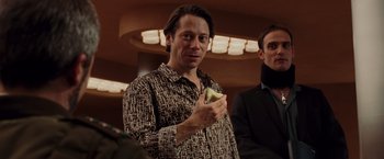 Movie still from “Quantum of Solace” (2008), directed by Marc Forster – A man holding a piece of food while standing next to another man; Close Up shot, Over the shoulder angle