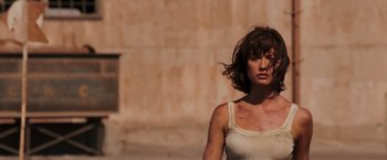Movie still from “Quantum of Solace” (2008), directed by Marc Forster – A woman in a white tank top standing in front of a building; Close Up shot, Low angle