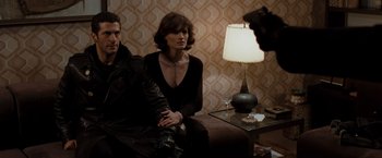 Movie still from “Quantum of Solace” (2008), directed by Marc Forster – A man and a woman sitting on a couch in front of a lamp; Medium shot, Over the shoulder angle