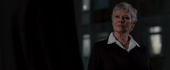 Movie still from “Quantum of Solace” (2008), directed by Marc Forster – An older woman wearing a black suit and white shirt; Close Up shot, Low angle