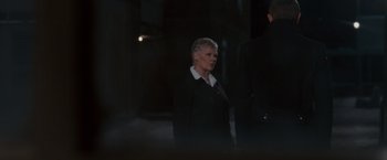 Movie still from “Quantum of Solace” (2008), directed by Marc Forster – An older woman wearing a suit and tie standing next to a man; Medium shot, Over the shoulder angle