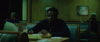 Movie still from “Queen & Slim” (2019), directed by Melina Matsoukas – A man sitting at a table with a plate of food in front of him; Medium shot, High angle