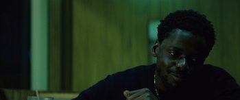 Movie still from “Queen & Slim” (2019), directed by Melina Matsoukas – A man eating a hot dog while sitting in a room; Close Up shot, Over the shoulder angle