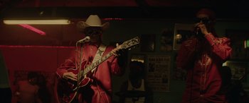 Movie still from “Queen & Slim” (2019), directed by Melina Matsoukas – A man in a cowboy hat playing a guitar in front of a microphone; Medium shot, Low angle