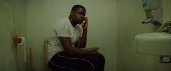 Movie still from “Queen & Slim” (2019), directed by Melina Matsoukas – A man sitting on a chair talking on a phone; Medium shot, High angle