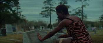 Movie still from “Queen & Slim” (2019), directed by Melina Matsoukas – A woman touching a tombstone in a cemetery; Medium shot, Over the shoulder angle
