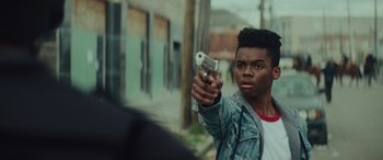 Movie still from “Queen & Slim” (2019), directed by Melina Matsoukas – A young man holding a gun while standing on the street; Close Up shot, Over the shoulder angle