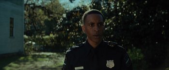 Movie still from “Queen & Slim” (2019), directed by Melina Matsoukas – A man in a police uniform standing in front of trees; Close Up shot, Low angle