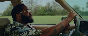 Movie still from “Queen & Slim” (2019), directed by Melina Matsoukas – A man driving a car in a grassy field; Close Up shot, Over the shoulder angle