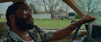 Movie still from “Queen & Slim” (2019), directed by Melina Matsoukas – A man driving a car in the grass; Close Up shot, Over the shoulder angle