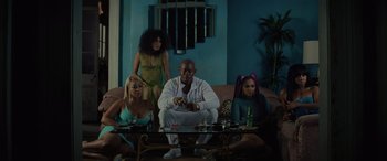 Movie still from “Queen & Slim” (2019), directed by Melina Matsoukas – A man sitting on top of a couch next to a group of women; Wide shot, Low angle
