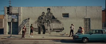 Movie still from “Queen & Slim” (2019), directed by Melina Matsoukas – A mural on the side of a building of a man and a woman sitting on the hood of a car; Wide shot, Low angle