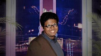 Movie still from “Queenmaker: The Making of an It Girl” (2023), directed by Zackary Drucker – A person wearing heart shaped glasses smiling for the camera; Close Up shot, High angle