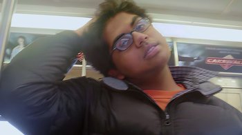 Movie still from “Queenmaker: The Making of an It Girl” (2023), directed by Zackary Drucker – A man with glasses is leaning on a cell phone; Close Up shot, Low angle